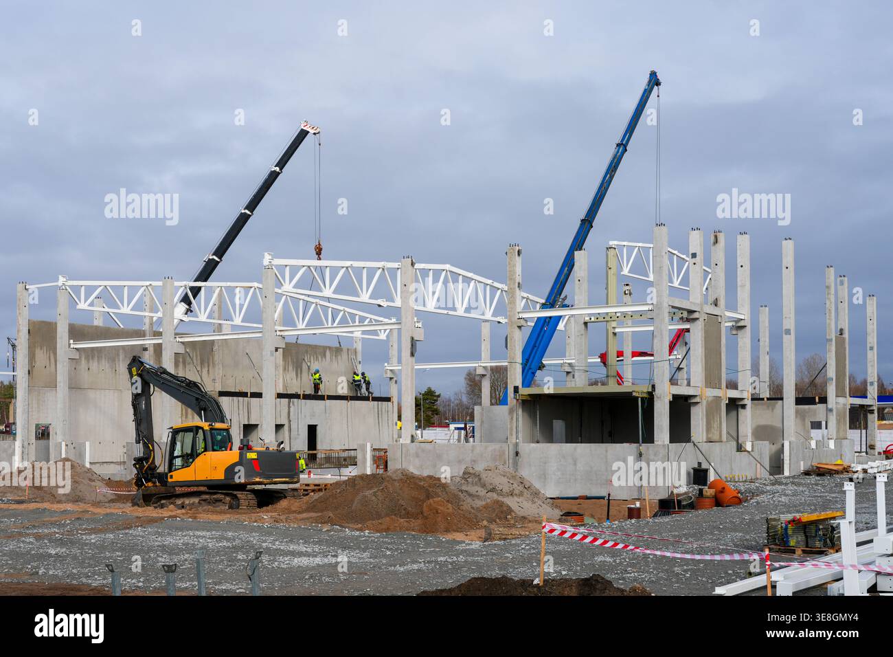 Gru e lavoratori montano travi in acciaio su strutture in calcestruzzo in cantieri attivi con macchinari Foto Stock