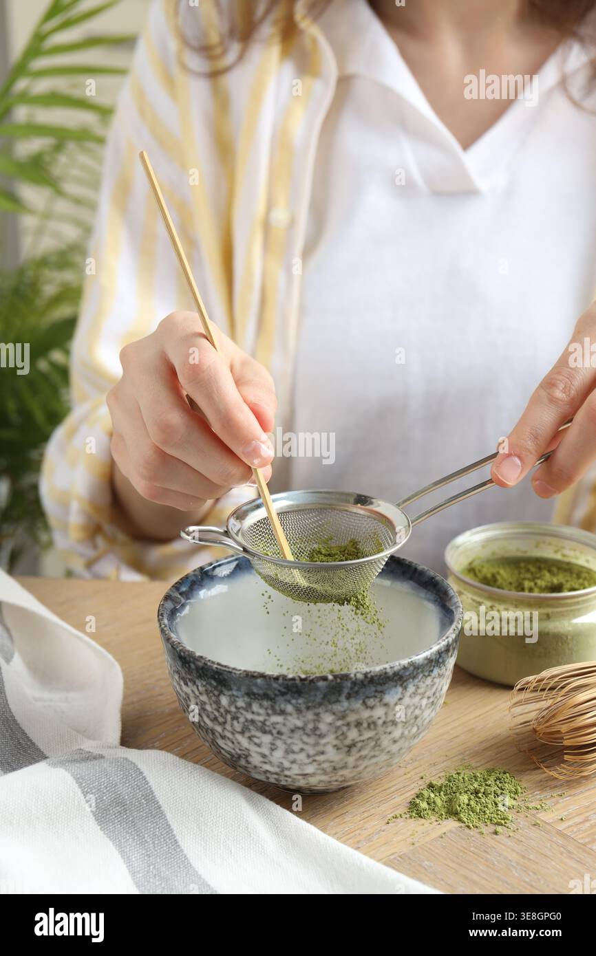 Donna setacciando polvere di matcha nel recipiente al tavolo di legno, primo piano Foto Stock