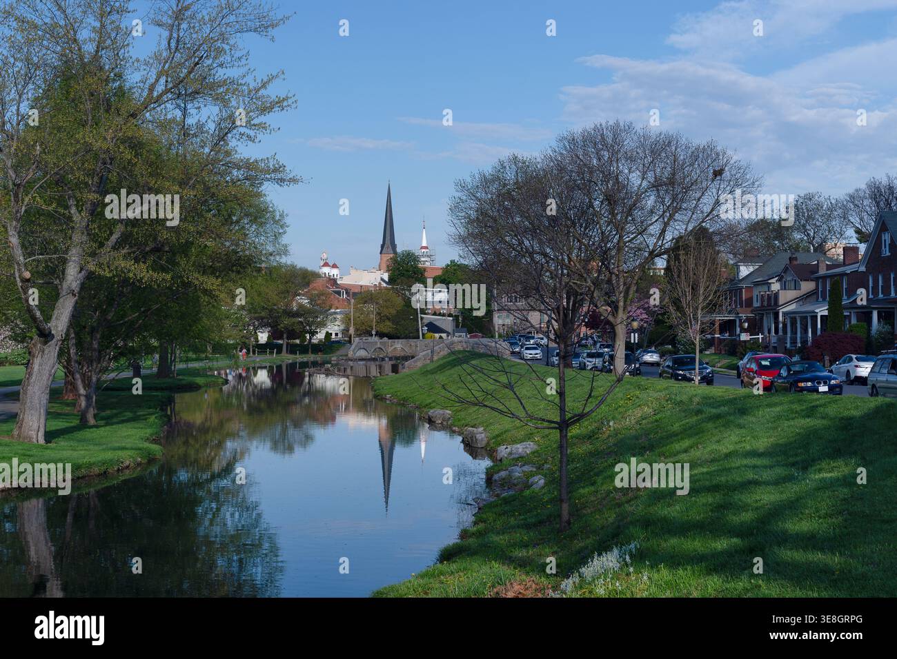 Vista panoramica di Carroll Creek a Frederick, Maryland, che riflette le storiche guglie della chiesa e i lussureggianti alberi verdi in una tranquilla serata primaverile. Foto Stock