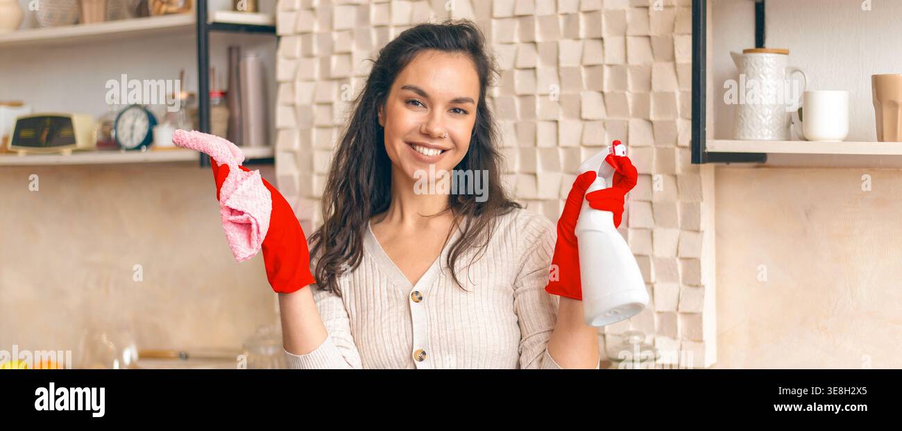 Donna che pulisce in cucina sorridendo con i materiali di pulizia Foto Stock