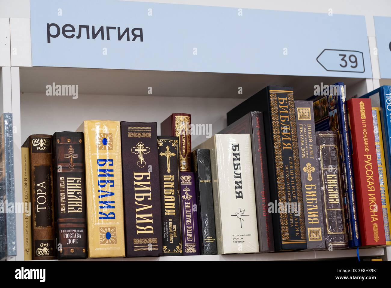 Mosca, Russia - 14 aprile 2026: Raccolta di libri religiosi tra cui Bibbie e Torah esposti su uno scaffale in una biblioteca sotto un cartello etichettato Foto Stock