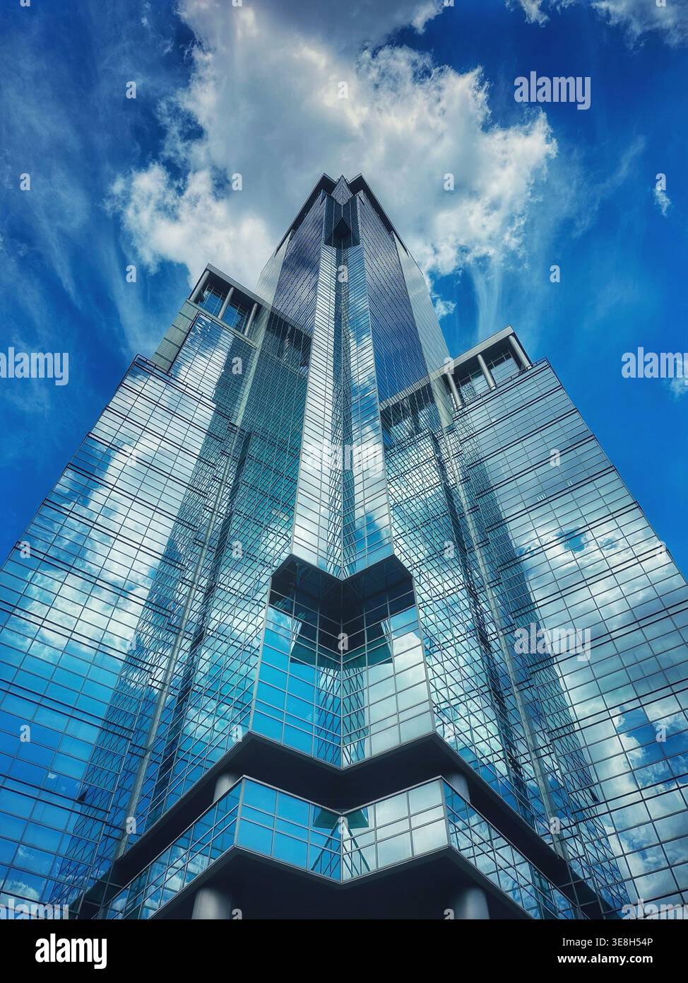 Un imponente grattacielo moderno dal design angolare guarda all'infinito cielo blu - Immagine stock catturata con smartphone