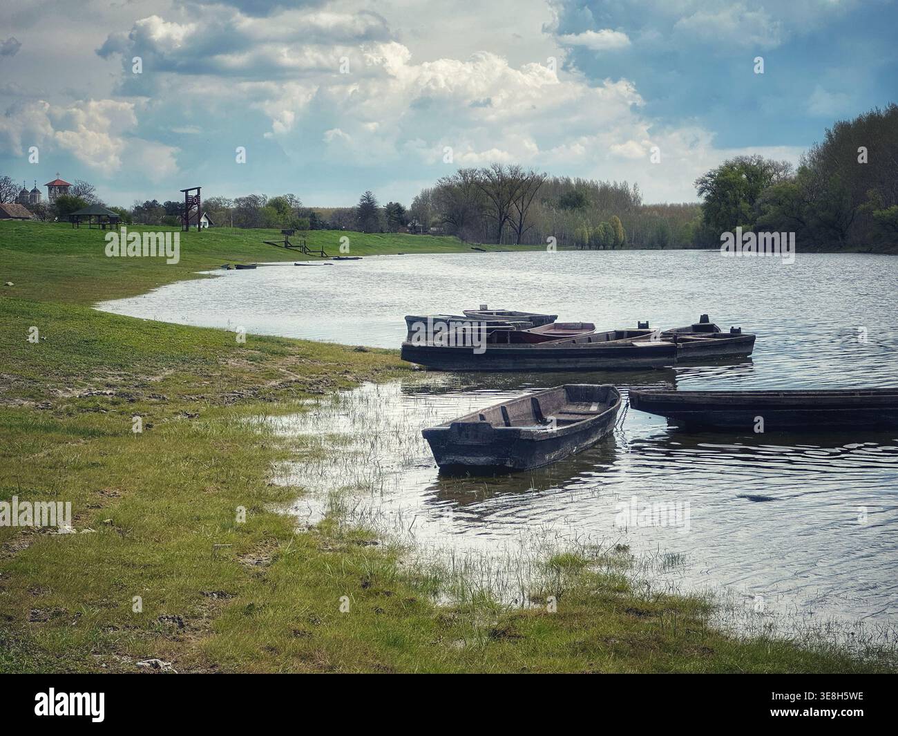 Barche ormeggiate sulla riva del lago con erba verde e cielo nuvoloso blu primaverile - Immagine stock catturata con smartphone