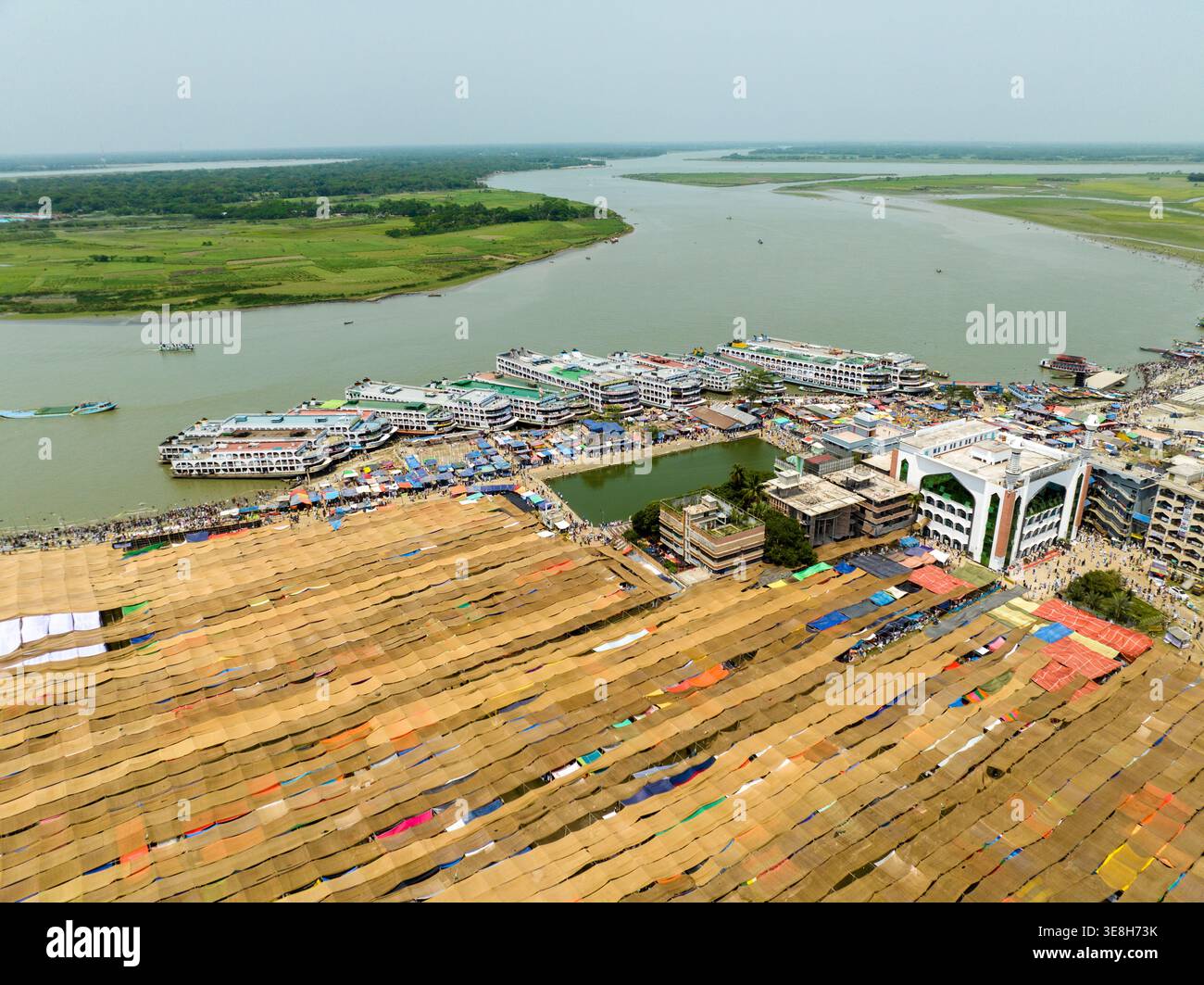 Vista aerea di vasti tappeti dorati che si asciugano sotto il sole, in contrasto con il tortuoso fiume e la moschea verde, Charmonai, Barisal Division, Bangladesh Foto Stock