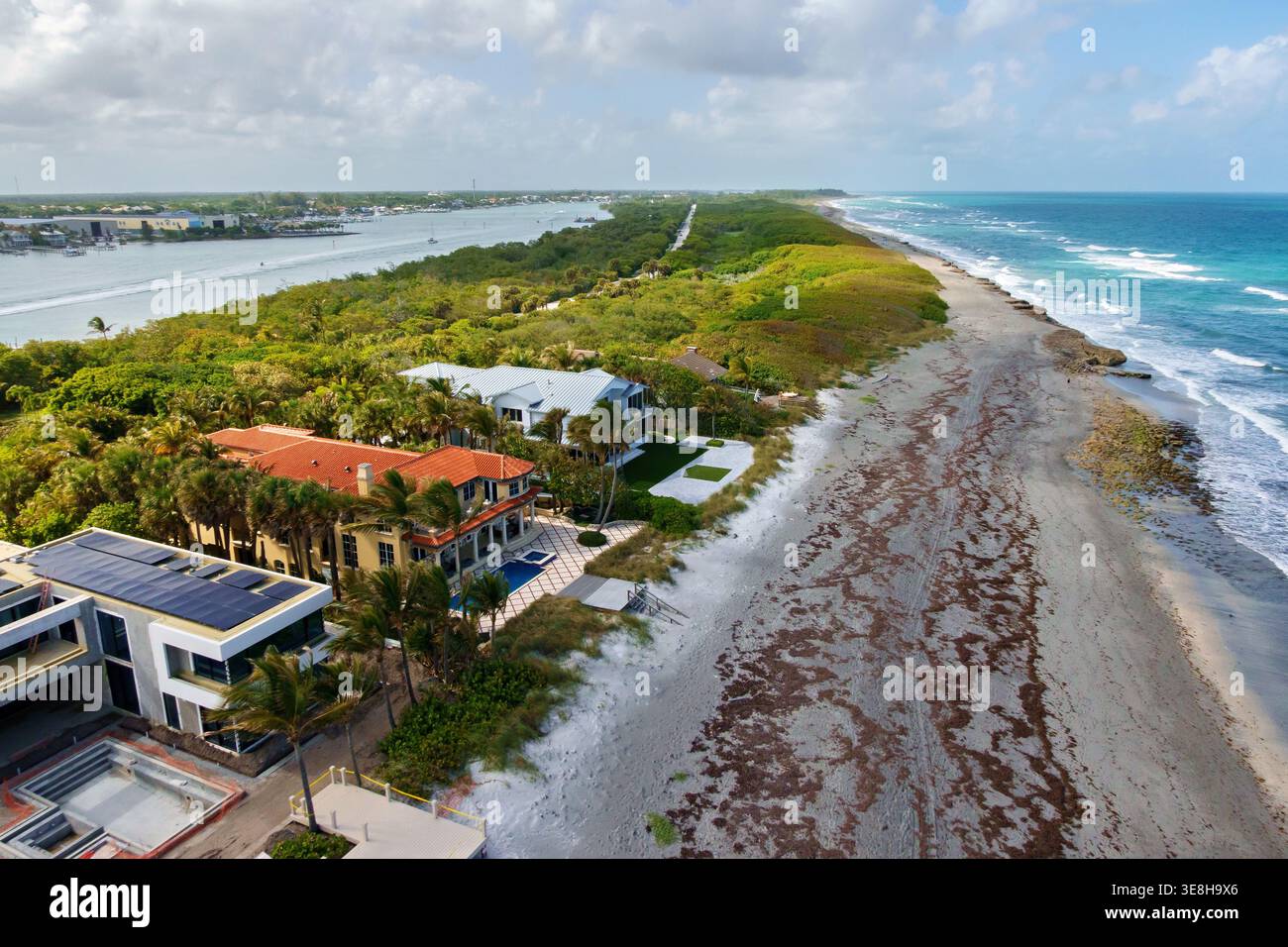 Vista aerea della costa, dove il mare blu profondo incontra la spiaggia sabbiosa, prospera una vegetazione lussureggiante e le case si stagliano elegantemente, l'isola di Giove, Foto Stock