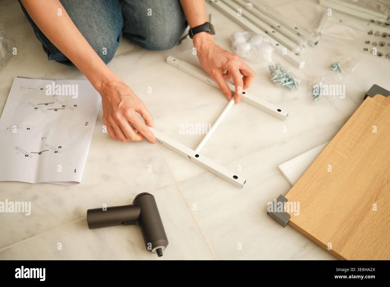 Donna che assembla mobili su pavimento in marmo con strumenti e istruzioni, miglioramento della casa e concetto di organizzazione Foto Stock