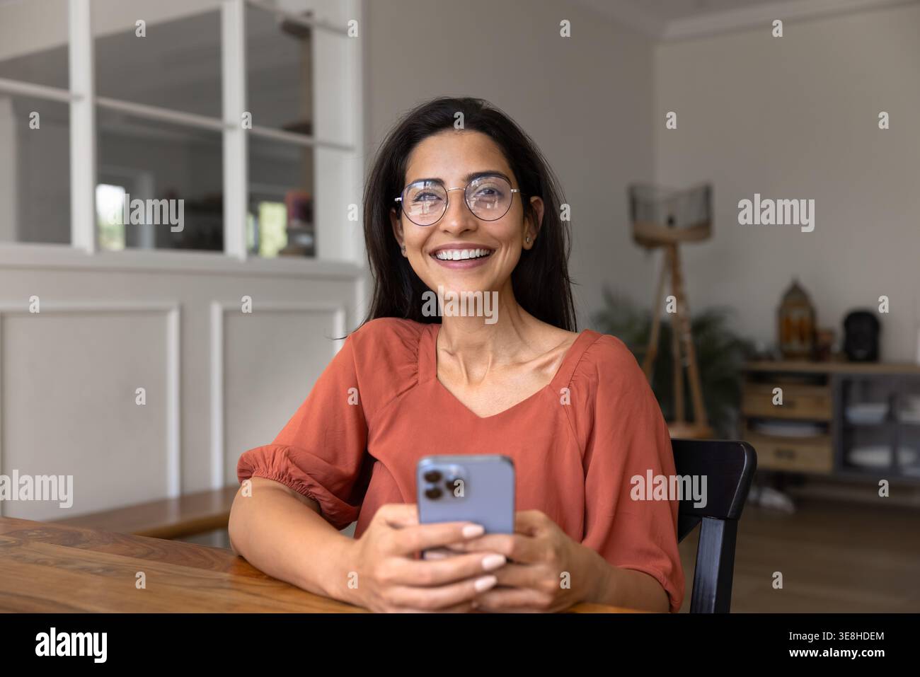 Ritratto di una donna brasiliana felice seduta alla scrivania utilizzando lo smartphone Foto Stock