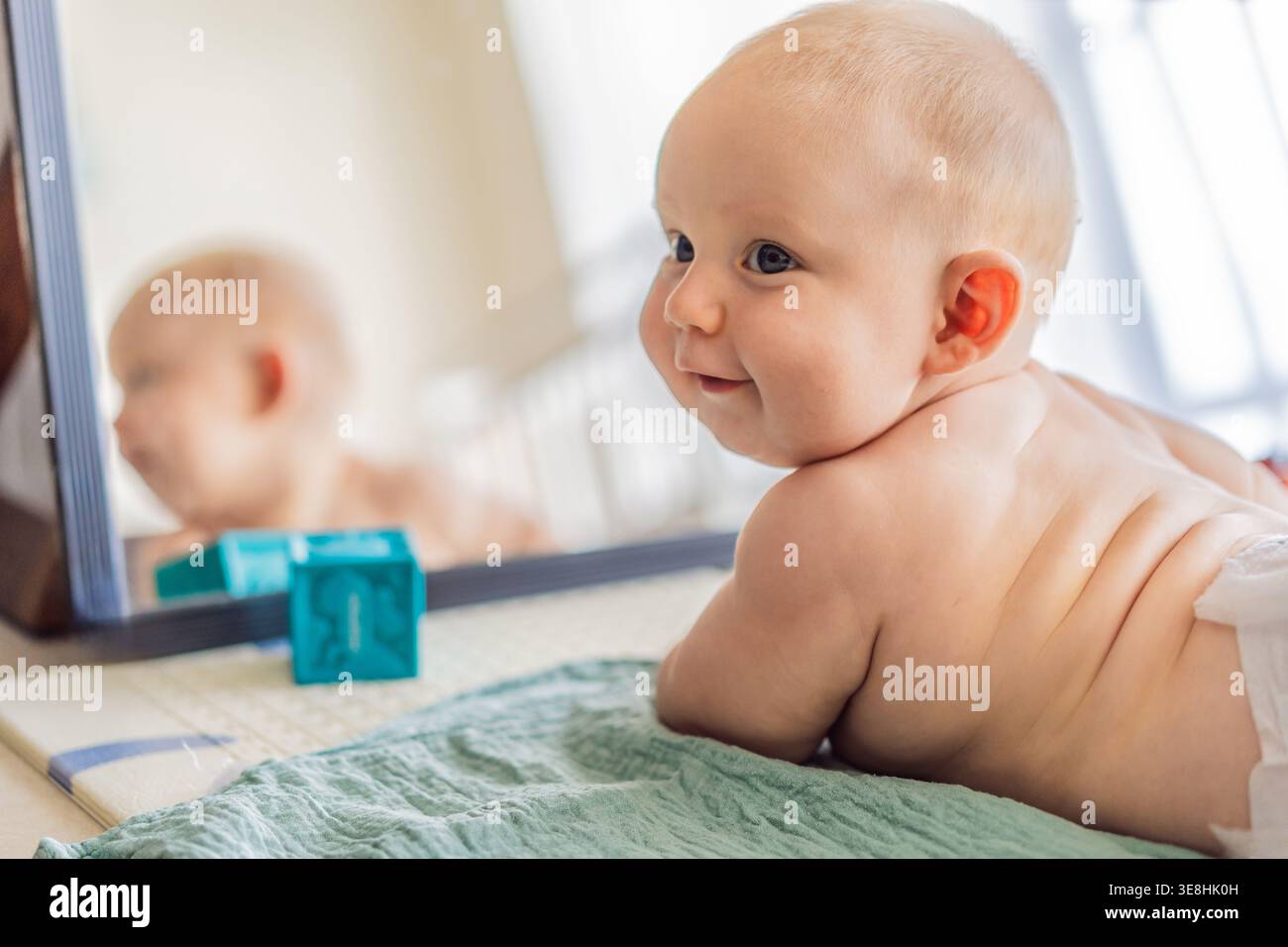 Il bambino sdraiato sul tappeto da gioco impara a gattonare e a salire su tutte le quattro. Neonato che pratica abilità motorie e sviluppo a casa. Crescita della prima infanzia Foto Stock