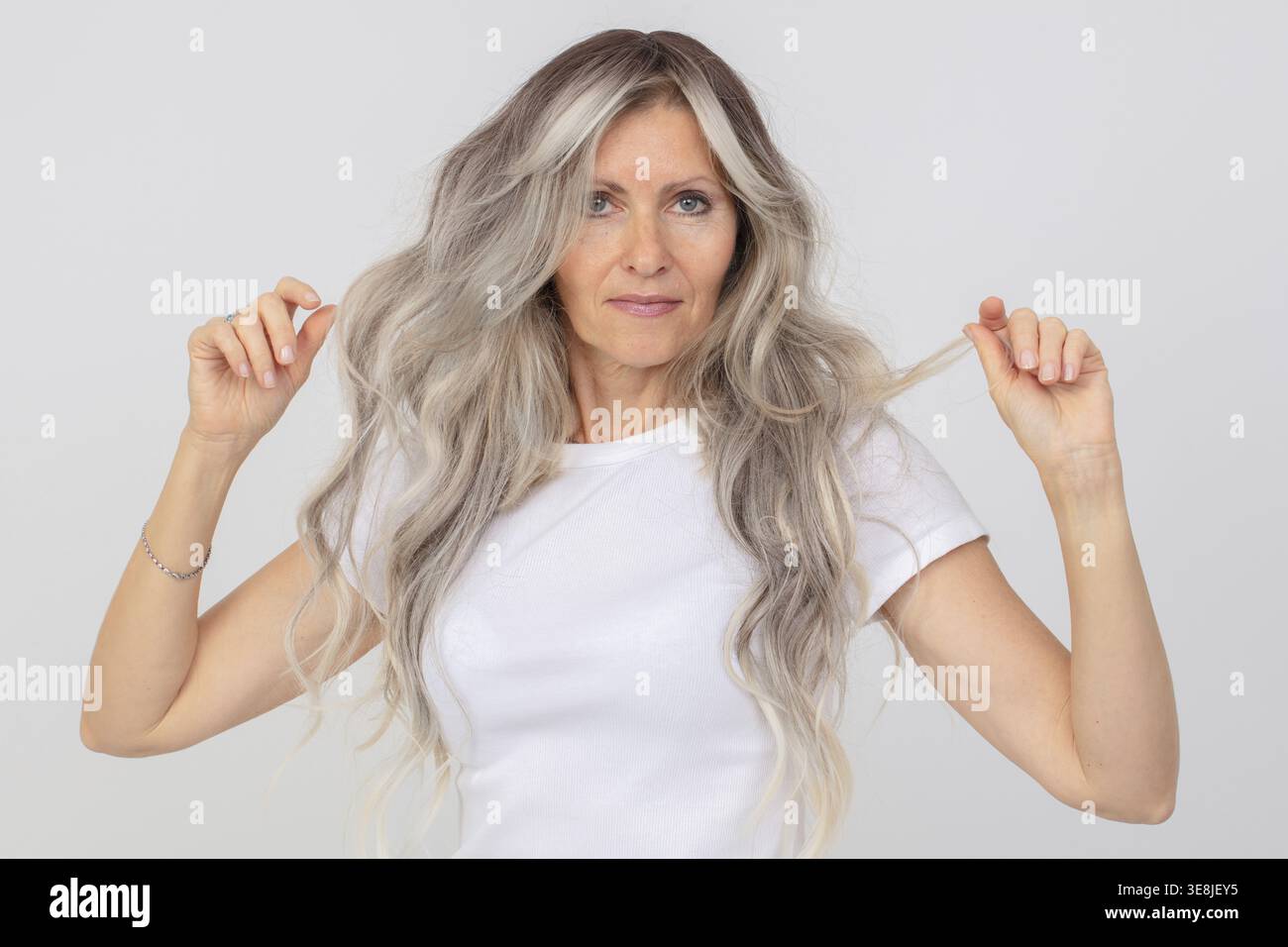Un'anziana donna dai capelli grigi con canotta bianca. Una signora anziana con capelli lunghi su sfondo bianco Foto Stock