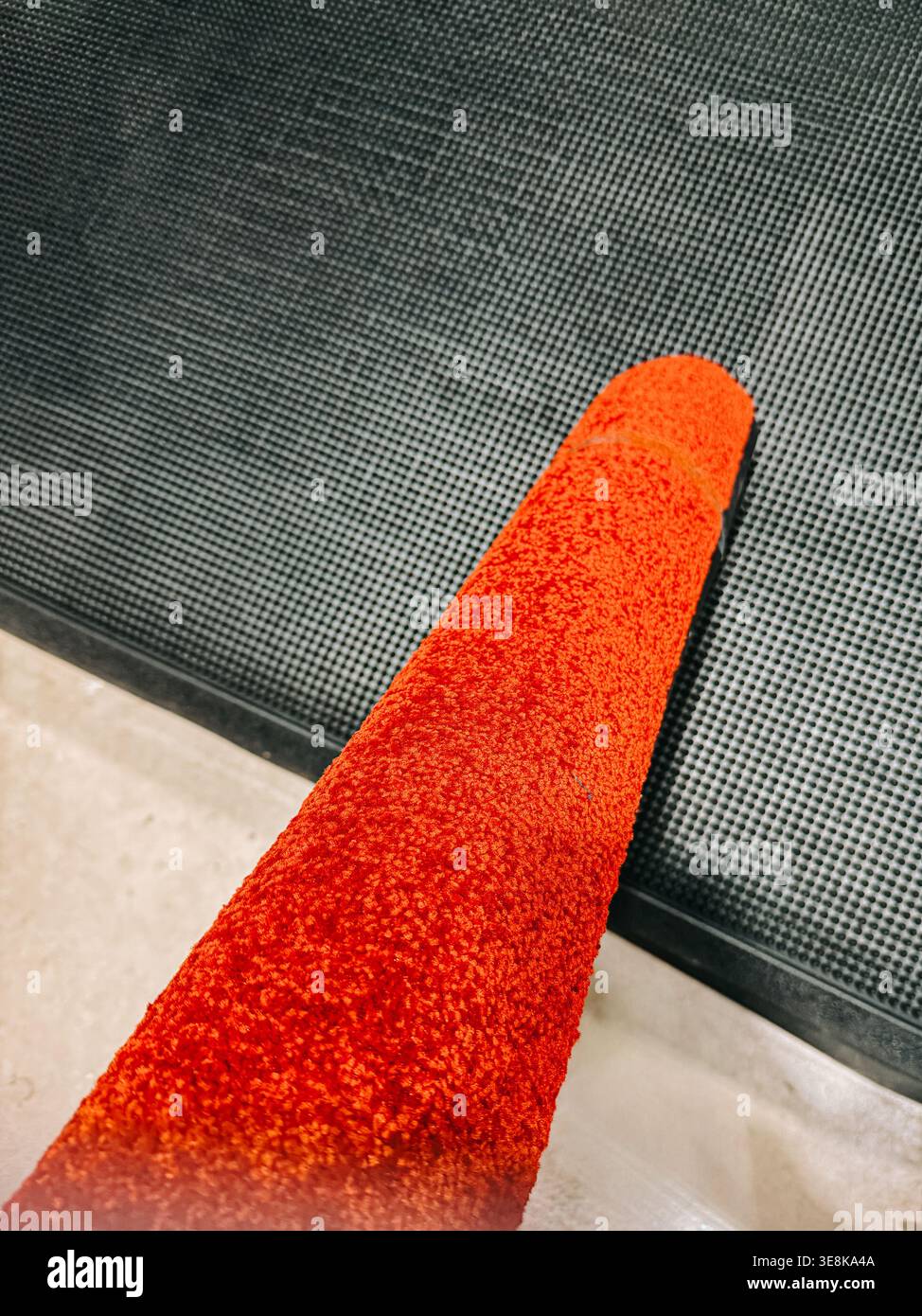 Vista macro di un rullo per pittura rosso brillante con un blocco testurizzato appoggiato su una superficie in gomma scura. Ideale per i concetti di ristrutturazione, miglioramento della casa, fai da te Foto Stock