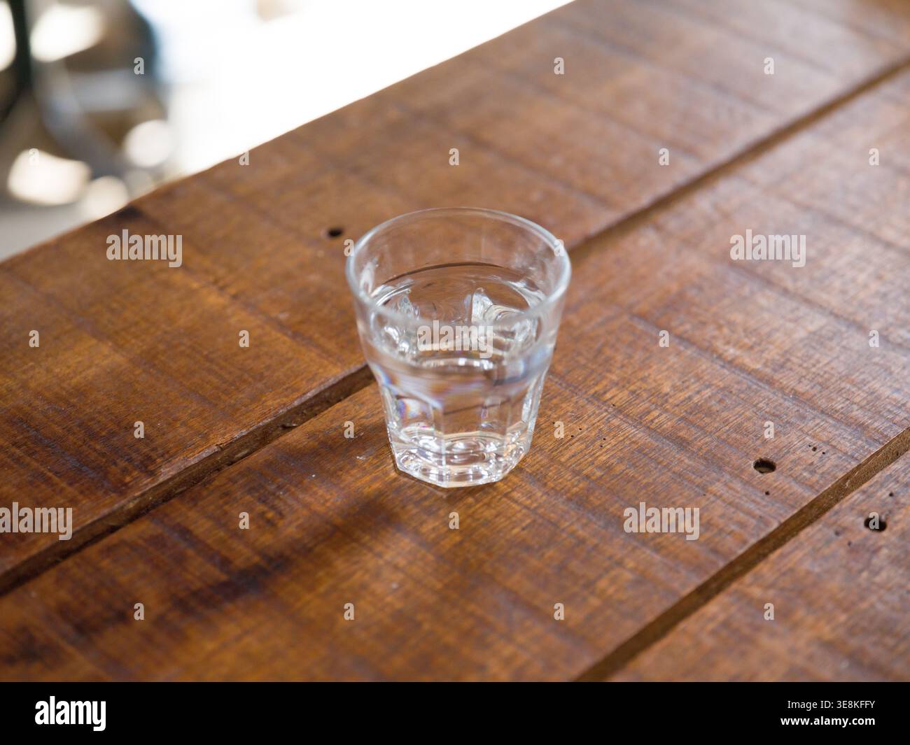Bicchiere d'acqua potabile su un tavolo da caffè in legno sopra la testa. Questa immagine presenta un bicchiere d'acqua, tavolo in legno minimalista. Un semplice bicchierino di vetro di trasparente d Foto Stock