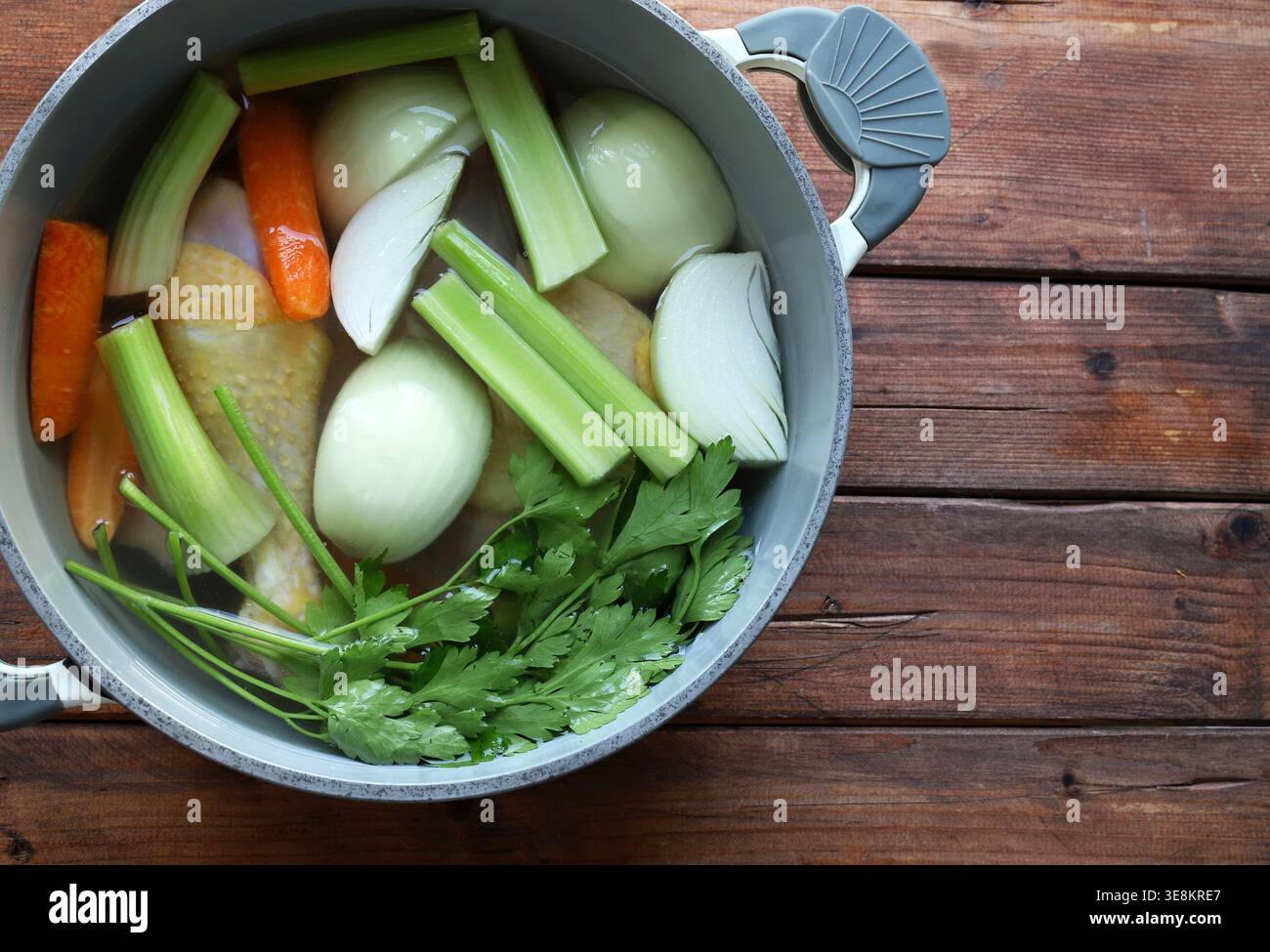 Preparare il tradizionale brodo di pollo con ingredienti biologici freschi in una pentola grigia su sfondo rustico. Concetto di cucina sana. Primo piano. Copia spazio Foto Stock