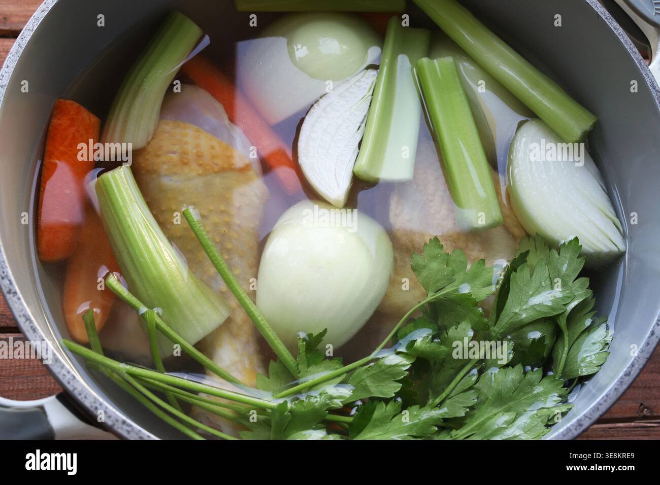 Preparare il tradizionale brodo di pollo con ingredienti biologici freschi in una pentola grigia su sfondo rustico. Concetto di cucina sana. Primo piano. Copia spazio Foto Stock
