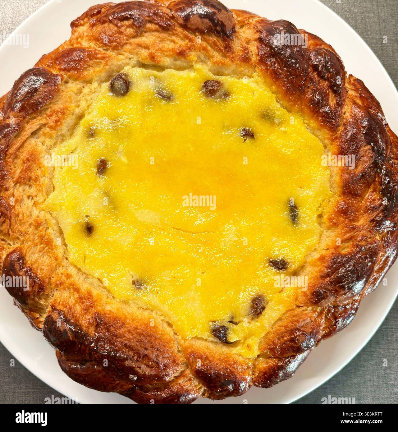 Pasca rumena tradizionale fatta in casa - torta al formaggio dolce pasquale ortodossa con uvetta e crosta di pasta intrecciata. Catturato come primo piano su un piatto bianco. Foto Stock
