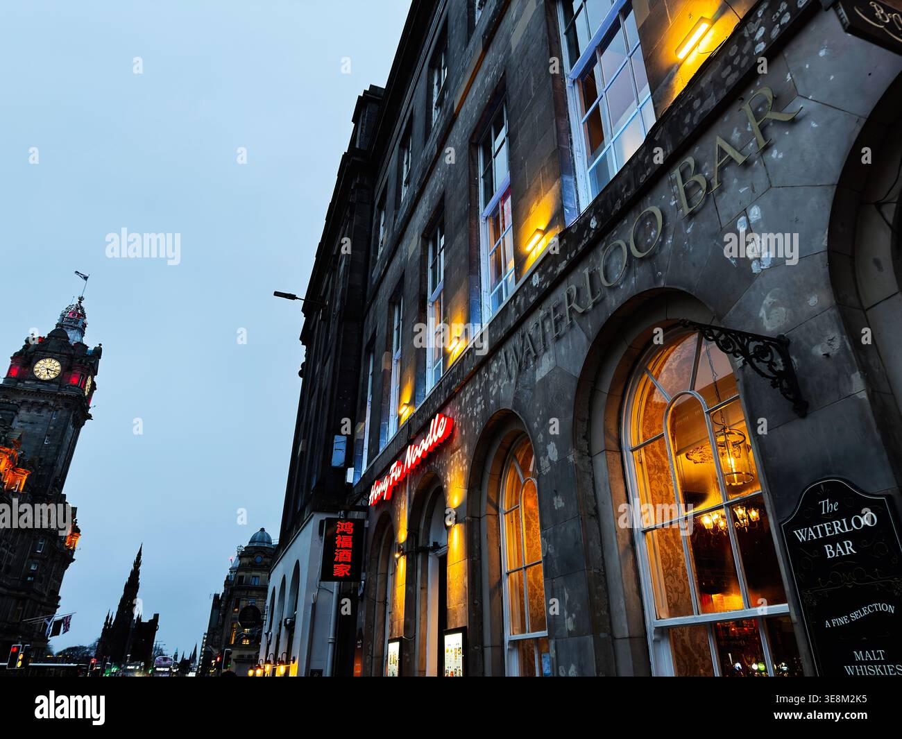 Edimburgo, Scozia, Regno Unito - 16 febbraio 2026: Scena urbana serale della facciata del Waterloo Bar con luci calde e torre dell'orologio distante a Edimburgo, S. Foto Stock
