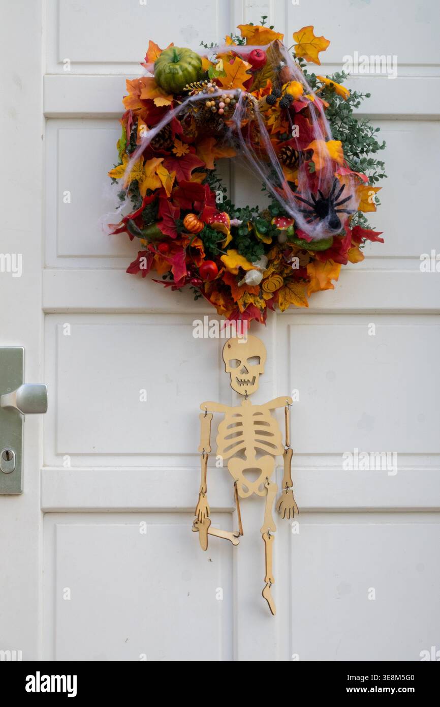 Corona di Halloween con foglie autunnali e decorazioni di scheletro in legno su una porta bianca Foto Stock