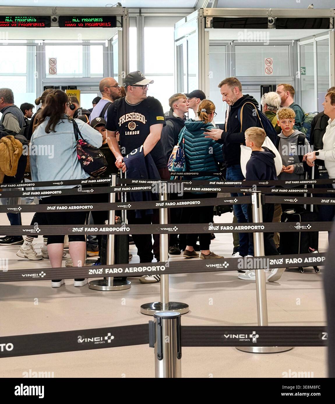 Passeggeri in attesa in una lunga fila al controllo dei passaporti presso l'aeroporto di Faro utilizzando il nuovo sistema EES che causa caos dei viaggi e ritardi del sistema di ingresso e uscita dell'UE - Immagine stock catturata con smartphone