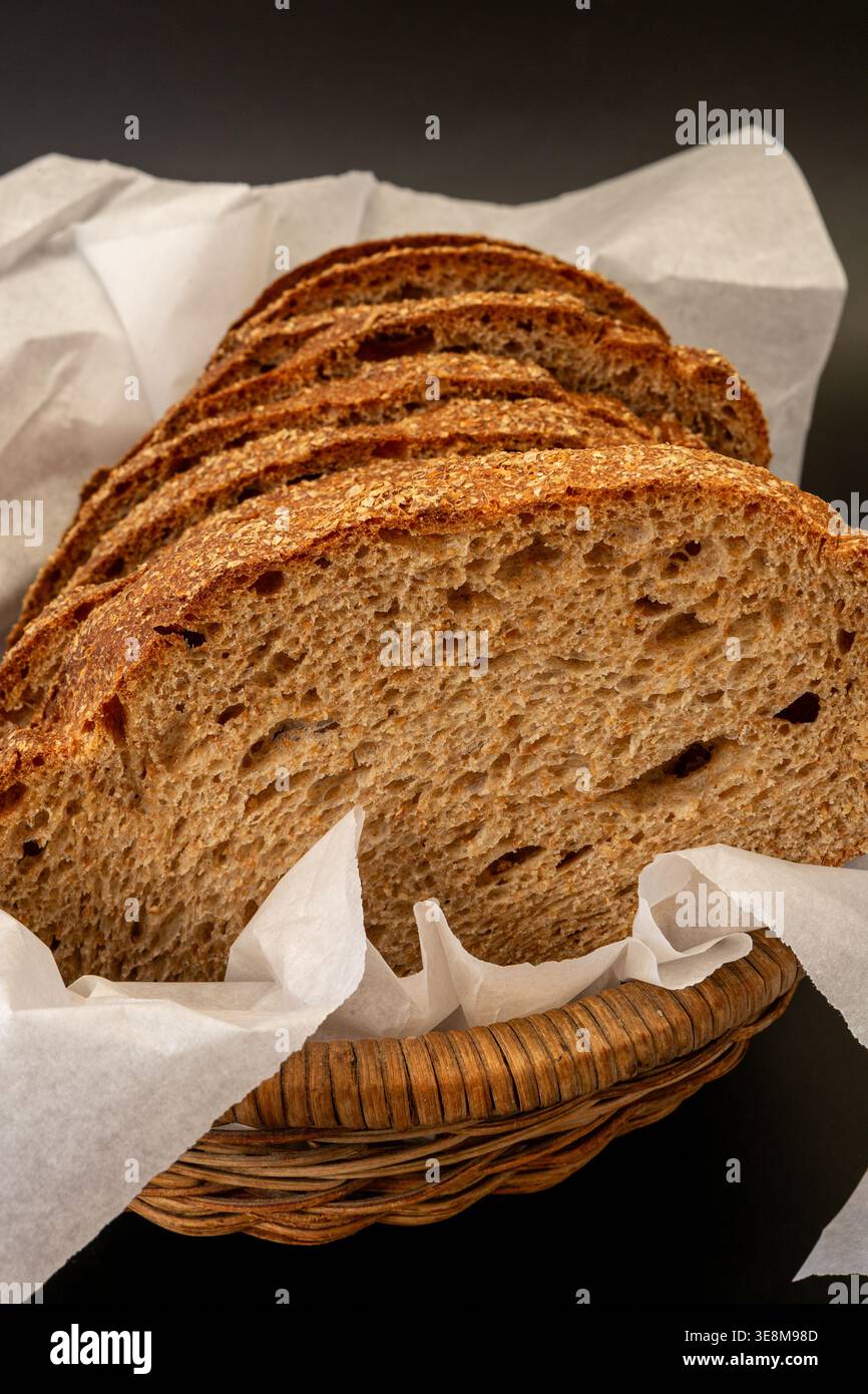 Vista ravvicinata del pane a fette presentato in un cestino in tessuto rivestito con carta pergamena bianca su sfondo nero minimalista. Foto Stock