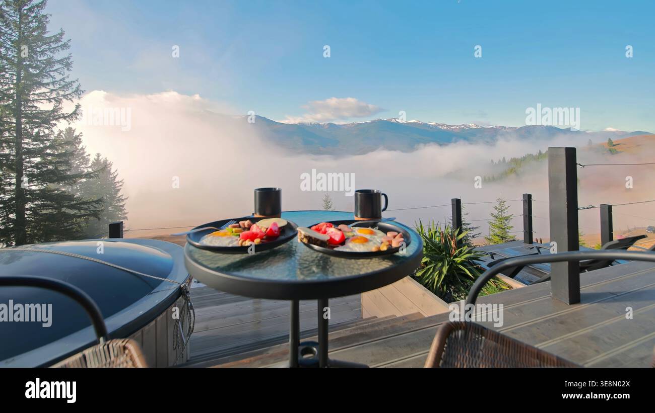 Colazione con vista sulle montagne sopra le nuvole. Colazione mattutina in terrazza con caffè, uova e frutta con vista sulle montagne nebbiose e sui pini Foto Stock