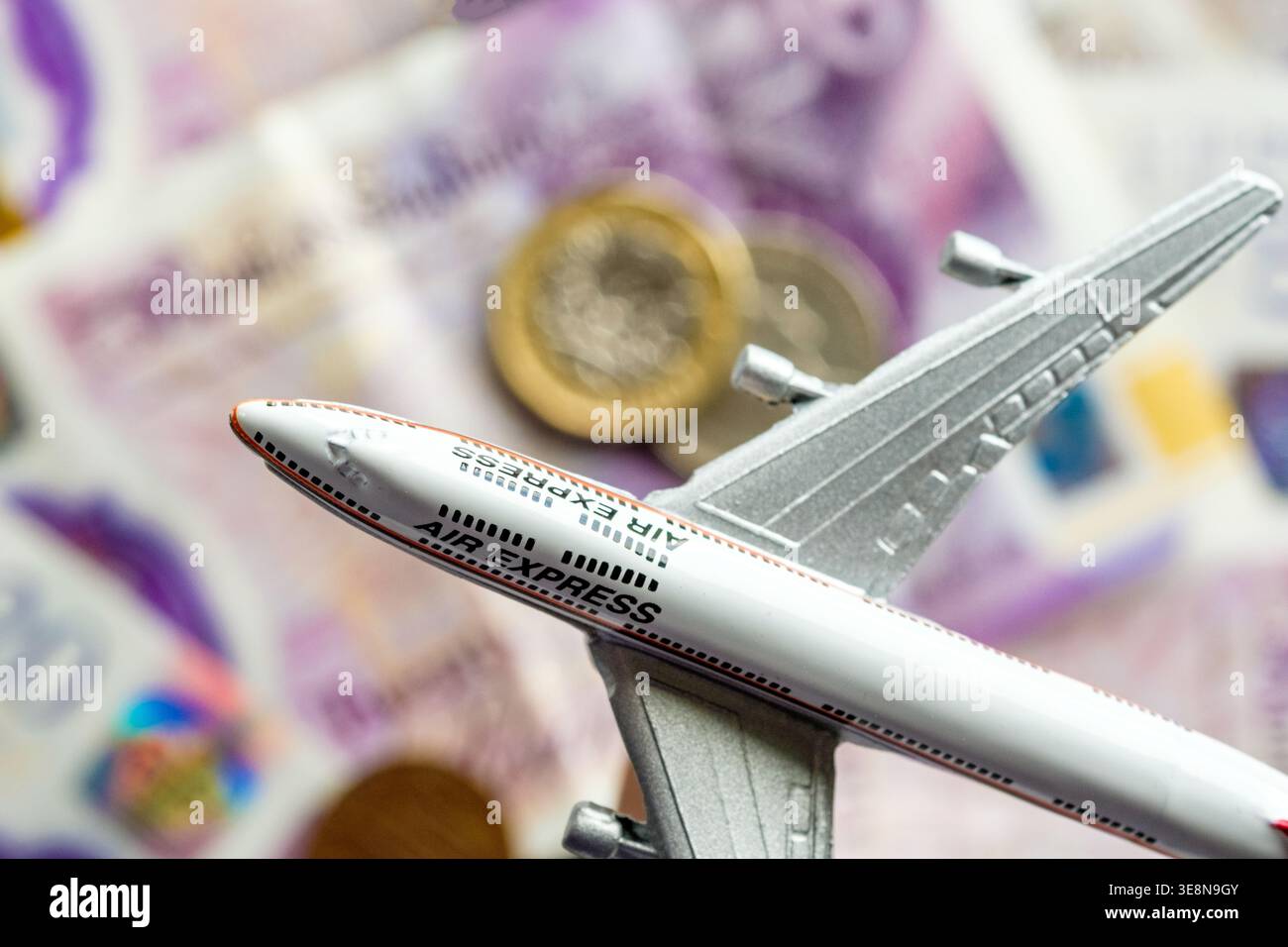 Concetto di costo del volo - un aereo giocattolo che vola sopra i soldi Foto Stock