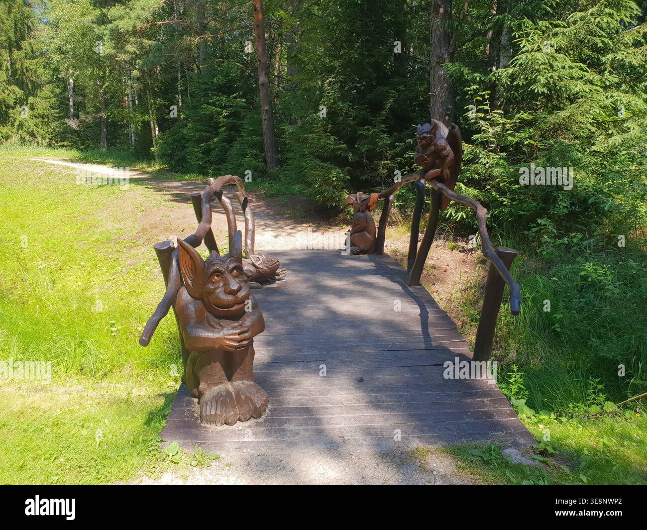 Ponte rustico in legno con stravaganti intagli di mitiche creature della foresta, tra cui un grande goblin sul davanti, annidato tra alti alberi verdi Foto Stock