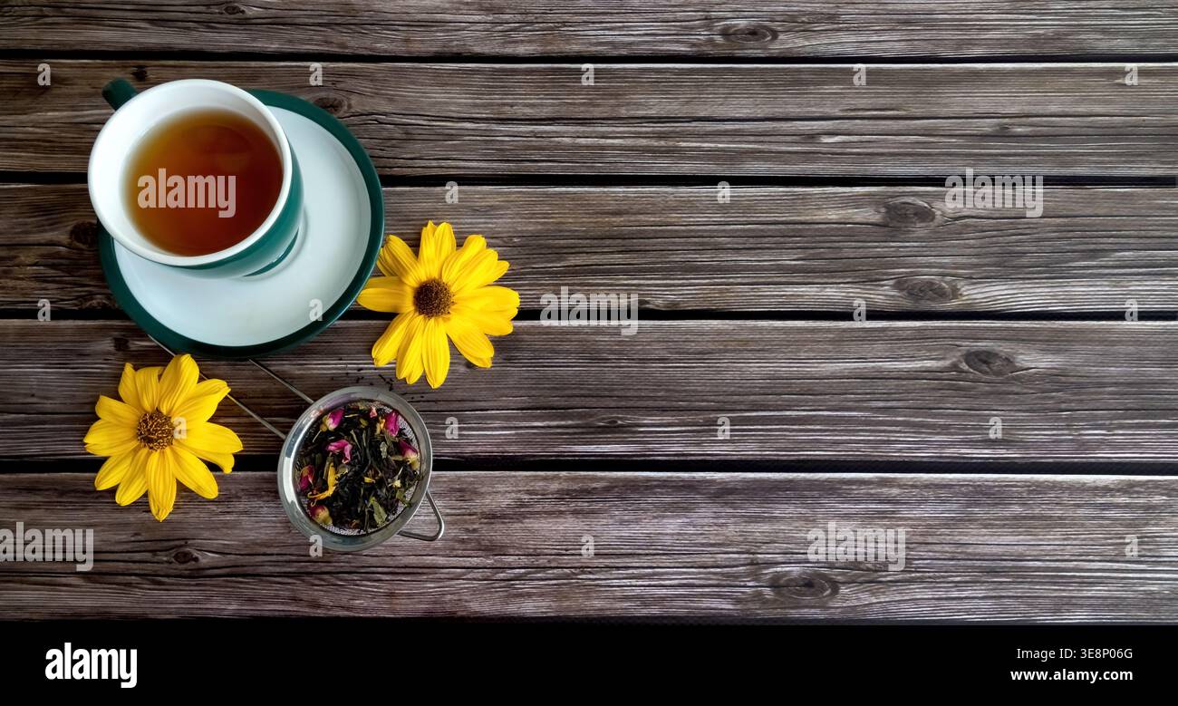 Tazza di tè con fiori su legno. Vista dall'alto di una tazza da tè con tè a foglie sciolte e fiori gialli luminosi su un rustico tavolo di legno con. Copia spazio. Foto Stock