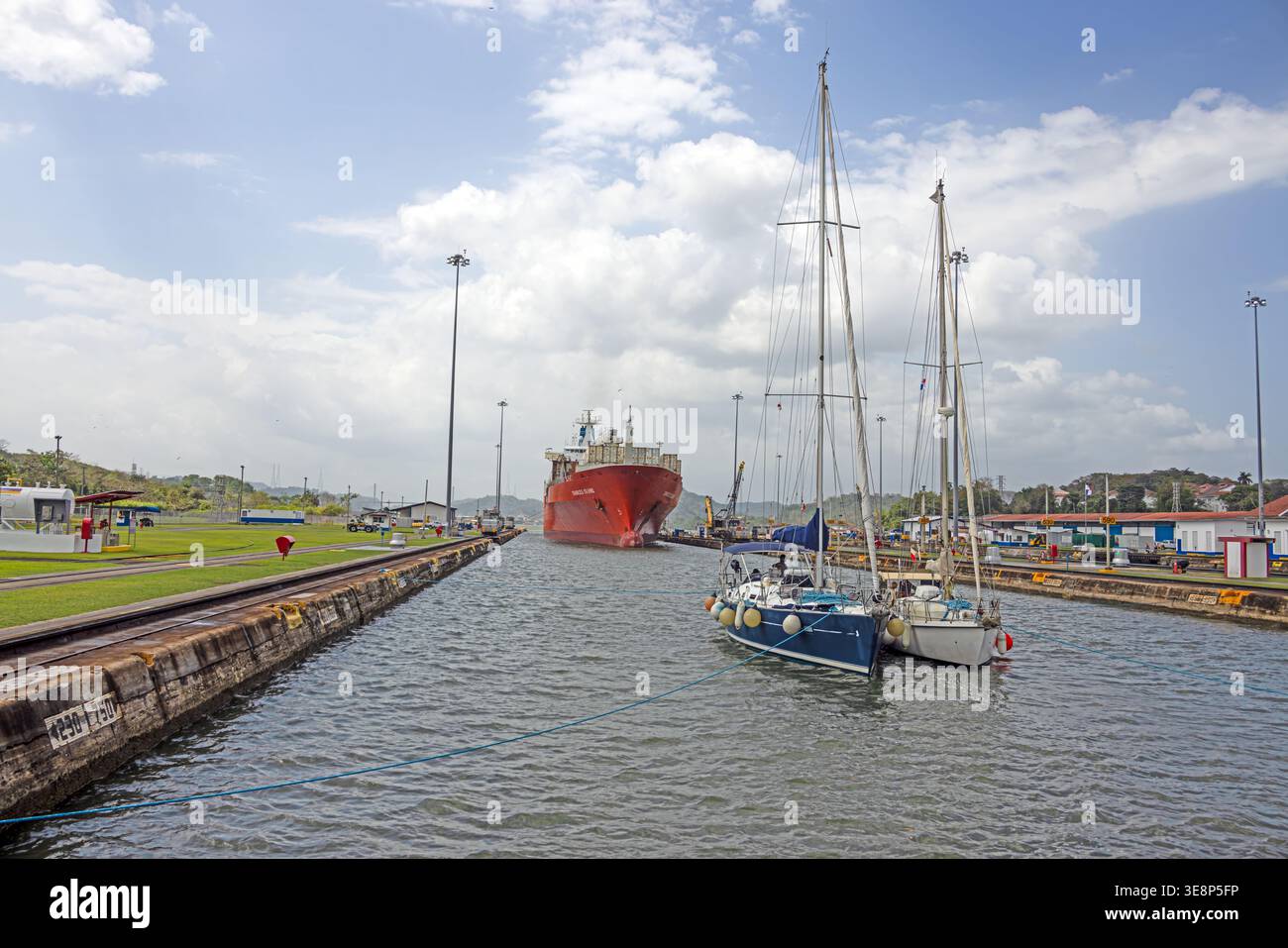 Barche a vela in attesa all'interno della chiusa del Canale di Panama con una grande nave da carico in avvicinamento sullo sfondo Foto Stock