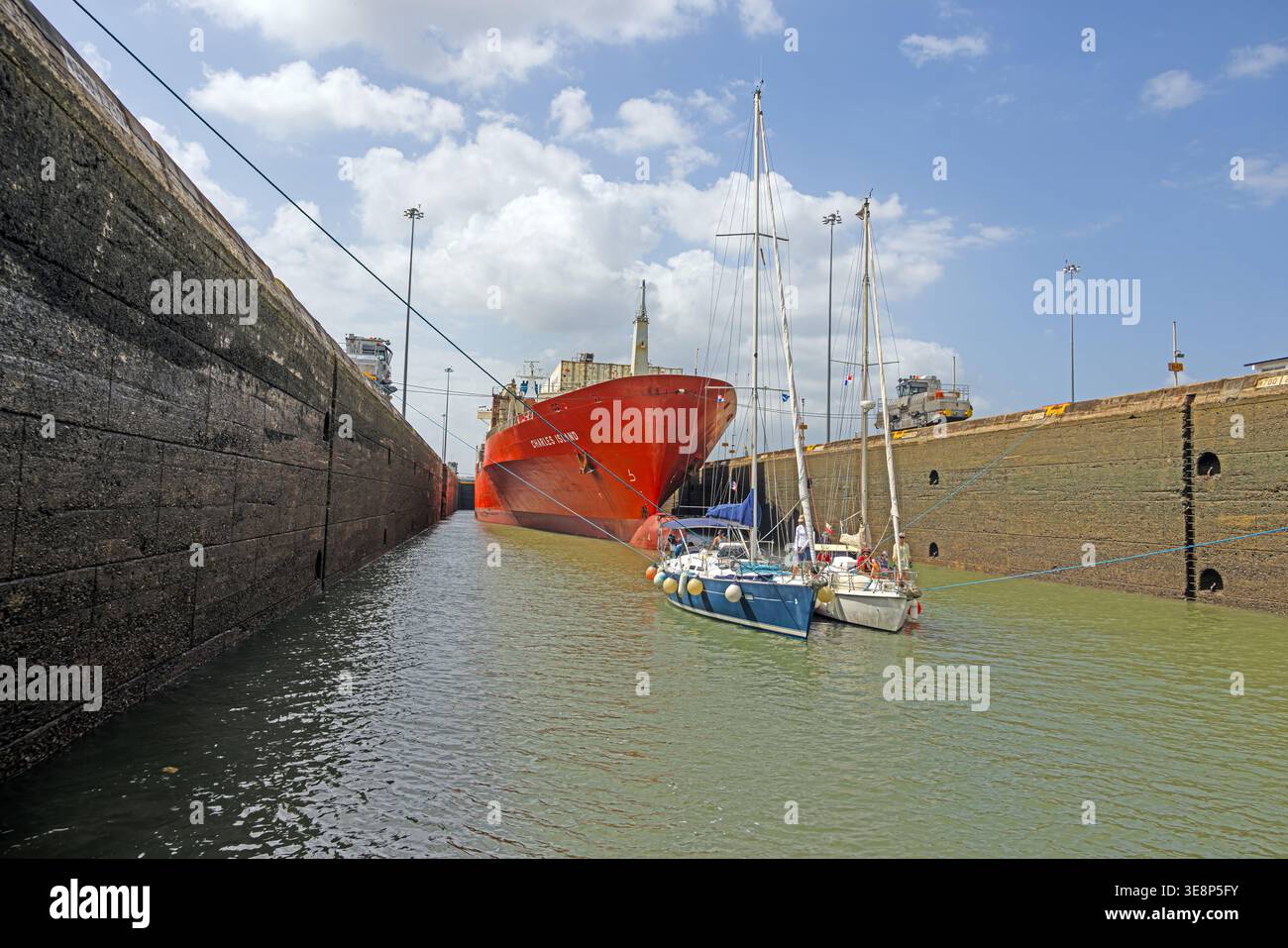 Grande nave da carico che condivide la camera di blocco del Canale di Panama con barche a vela che mostrano scala e navigazione Foto Stock