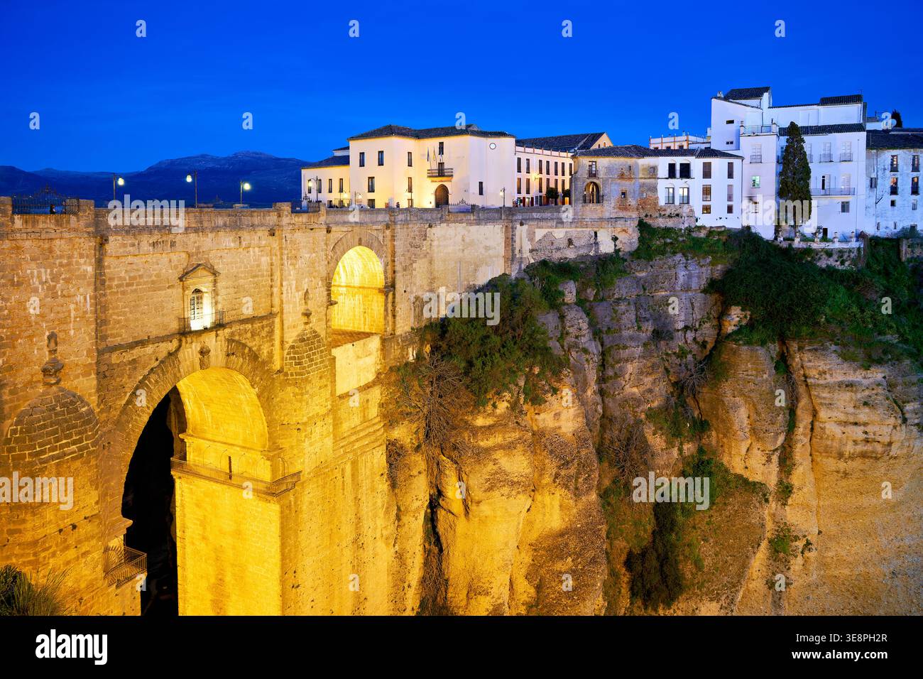 Ronda mostra il suo fascino di notte con edifici illuminati e la profonda gola di El Tajo. Il ponte collega i due lati della città. Foto Stock