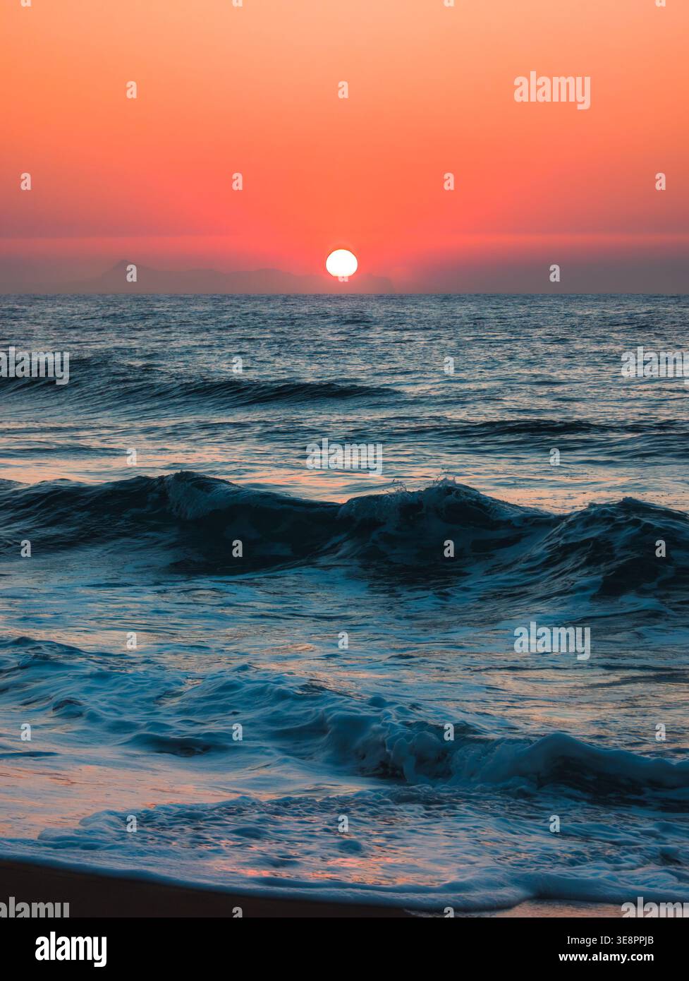 Tramonto sulle onde dell'oceano con montagne lontane a Rethymno, Grecia - Immagine stock catturata con smartphone