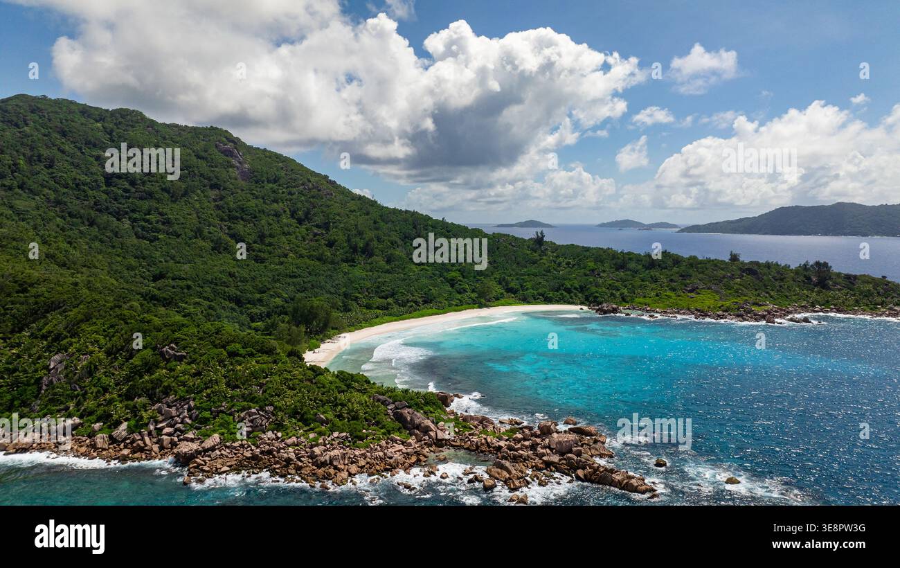 Verdi colline che si affacciano su una spiaggia di sabbia bianca con onde turchesi dell'oceano e cielo blu. Piccola Anse. Seychelles, la Digue. Foto Stock