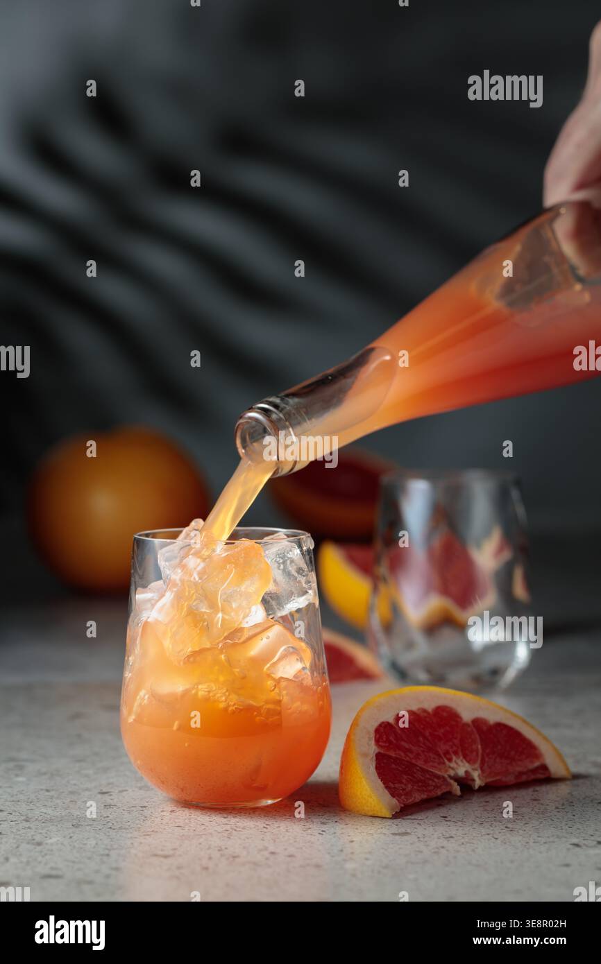 Il succo di pompelmo viene versato in un bicchiere con ghiaccio. Bere in un bicchiere congelato e frutta fresca su un tavolo di pietra. Sullo sfondo, le ombre del palmo leav Foto Stock