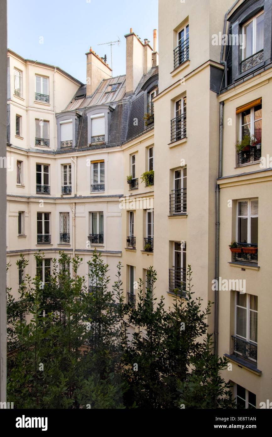 Vista del cortile di Parigi di un blocco residenziale con pareti color crema, tetto in mansarda e finestre dormitori, barre di ferro battuto per balconi Foto Stock