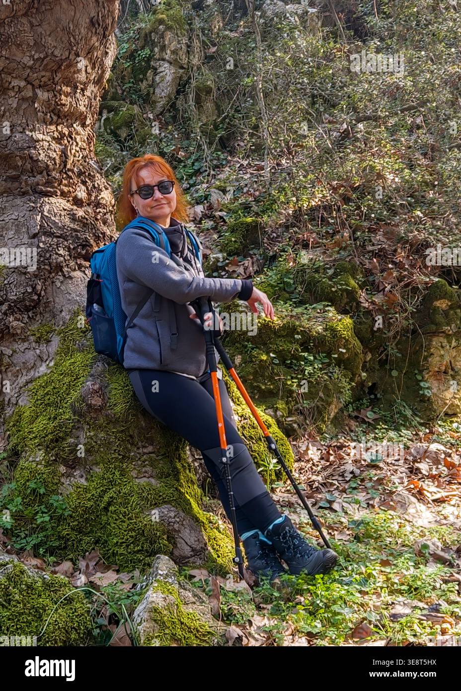 Ritratto ravvicinato di una donna sorridente, con occhiali da sole e bastoncini da trekking appoggiati su un albero muschiato. Stile di vita attivo e concetto di benessere. Turchia. Foto Stock