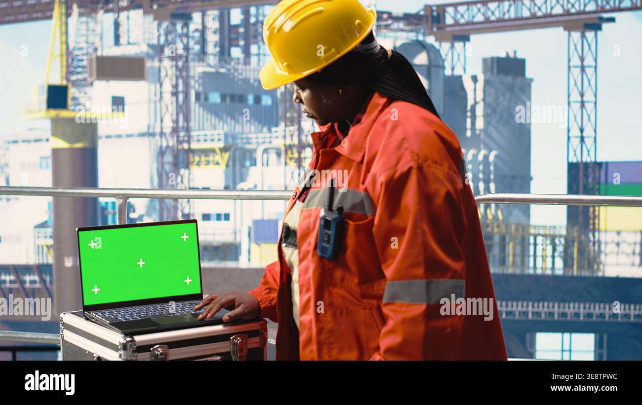 Computer portatile con schermo verde utilizzato dal lavoratore della macchina perforatrice che tiene in mano un dispositivo radio portatile per monitorare il funzionamento. Donna sul ponte piattaforma offshore che utilizza walkie talkie e un notebook mockup, per calibrare le attrezzature Foto Stock