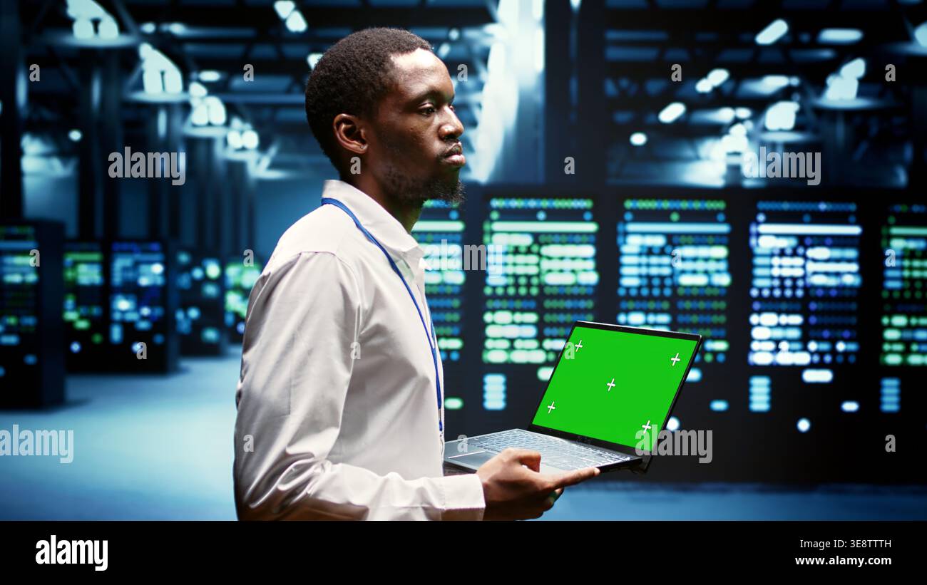 Ingegnere che utilizza un notebook con schermo verde per eseguire la manutenzione su server di gioco dedicati ad alta larghezza di banda utilizzati per gestire il traffico in arrivo degli utenti online che si uniscono da sedi in tutto il mondo. Foto Stock