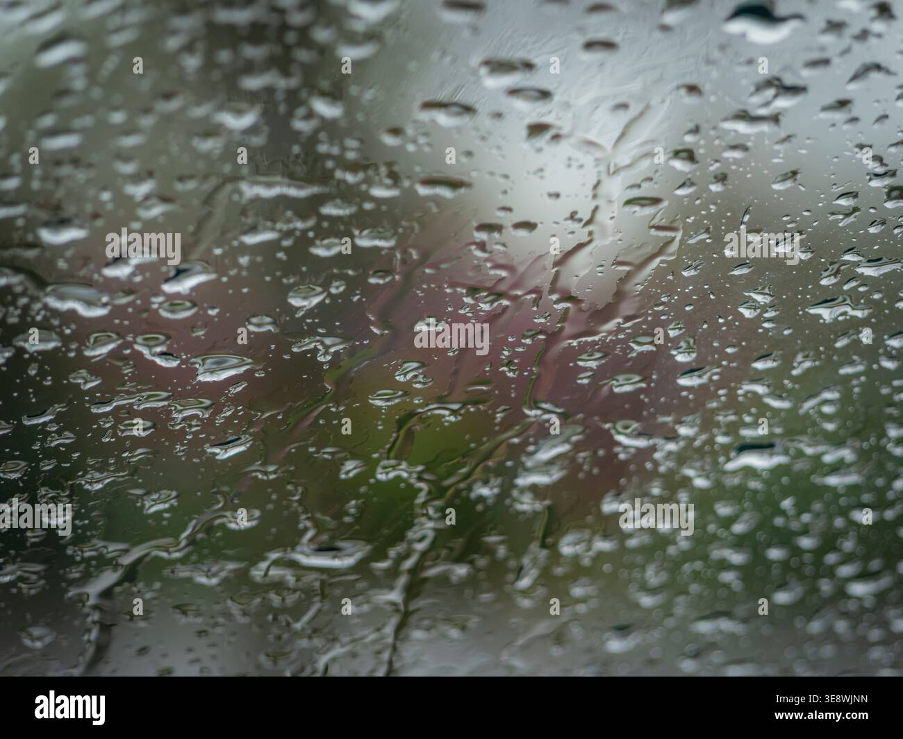 forti gocce di pioggia e strisce d'acqua su una superficie di vetro su un morbido sfondo bokeh di colori e luci sfocati Foto Stock