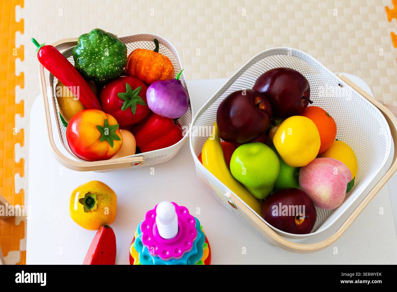 Due cestelli in rete traboccano di frutta e verdura colorate in plastica su un tavolo per bambini in una sala giochi che offre materiali per la selezione e il conteggio Foto Stock