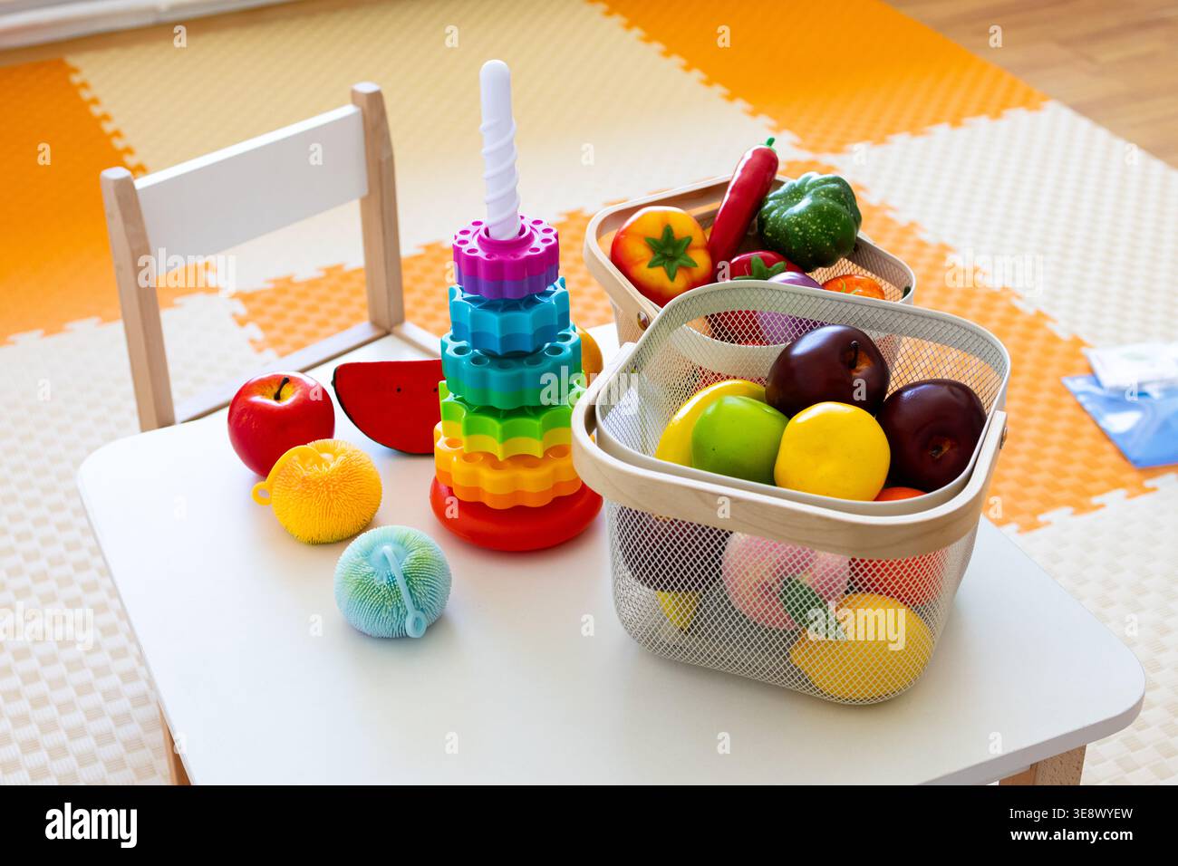 Un piccolo tavolo con sedia ospita una torre arcobaleno, due cesti di alimenti giocattolo e palle testurizzate che creano una vivace stazione prescolare per lo smistamento Foto Stock