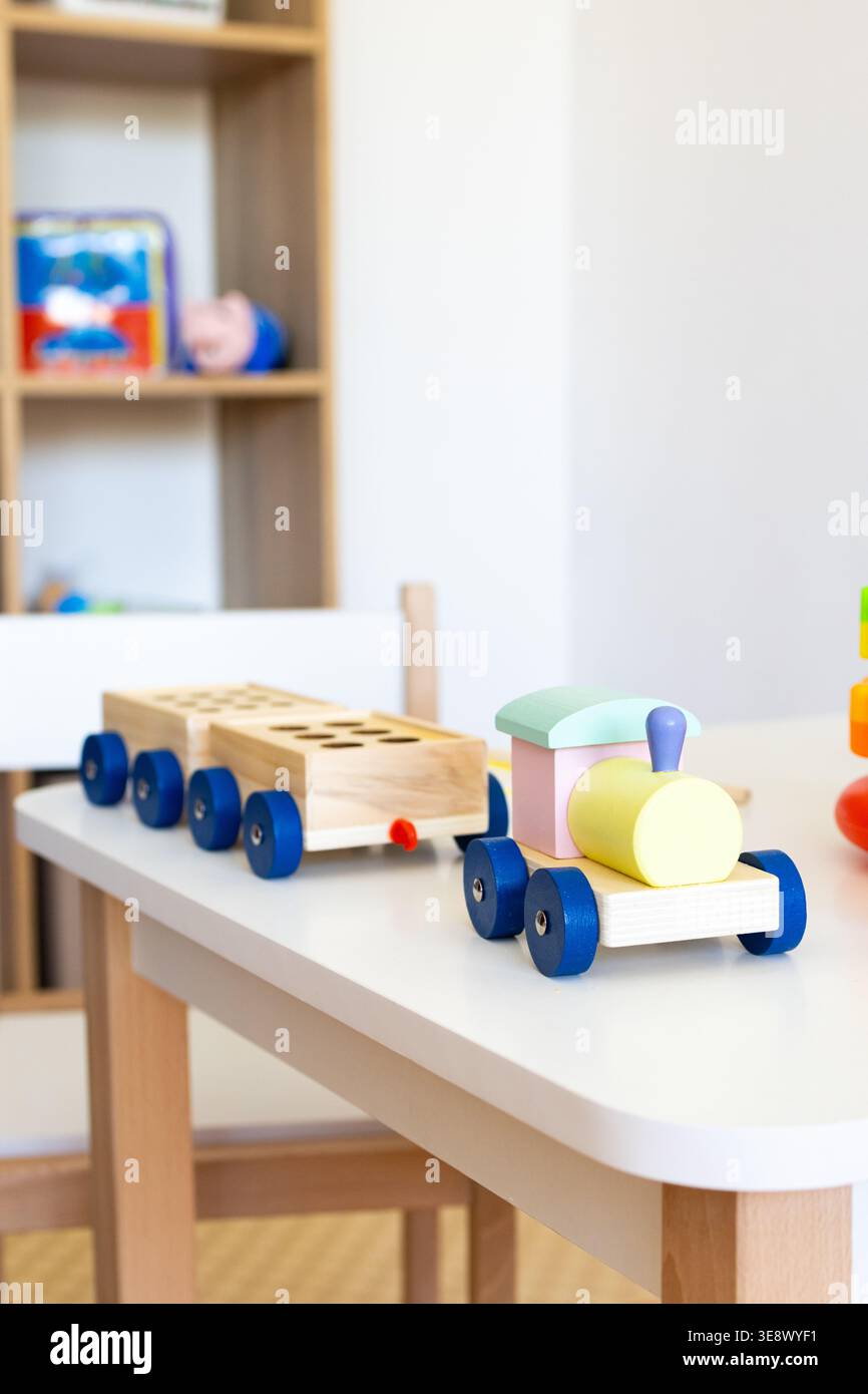 Vista verticale di un treno in legno pastello su un tavolo prescolare con carrozze pronte per il gioco, evidenziando materiali tattili e colori delicati in una calma Foto Stock