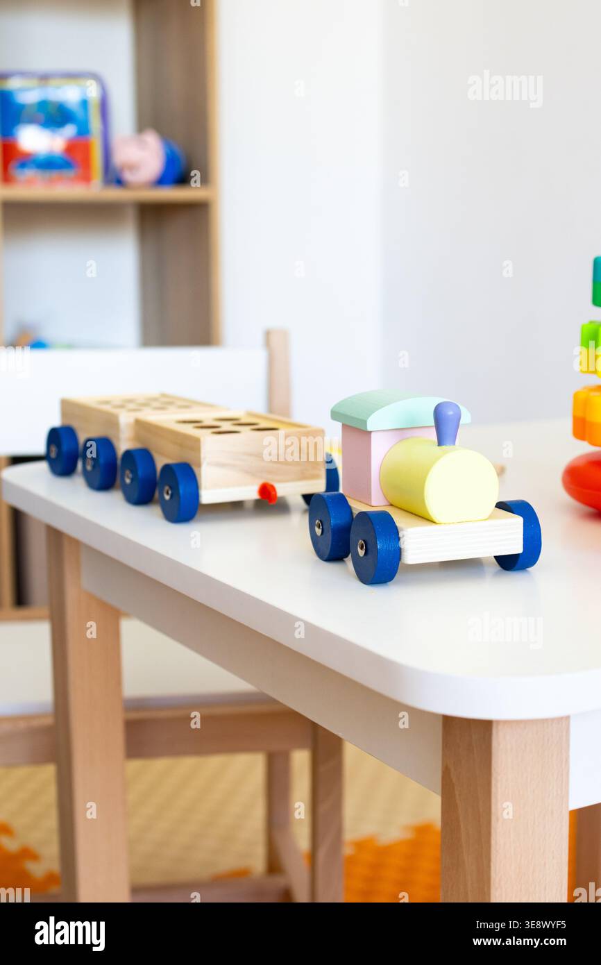 Il motore e il carro in legno pastello poggiano su una scrivania per bambini mentre una colorata torre si sovrappone all'inquadratura creando una divertente vignetta per l'apprendimento precoce Foto Stock