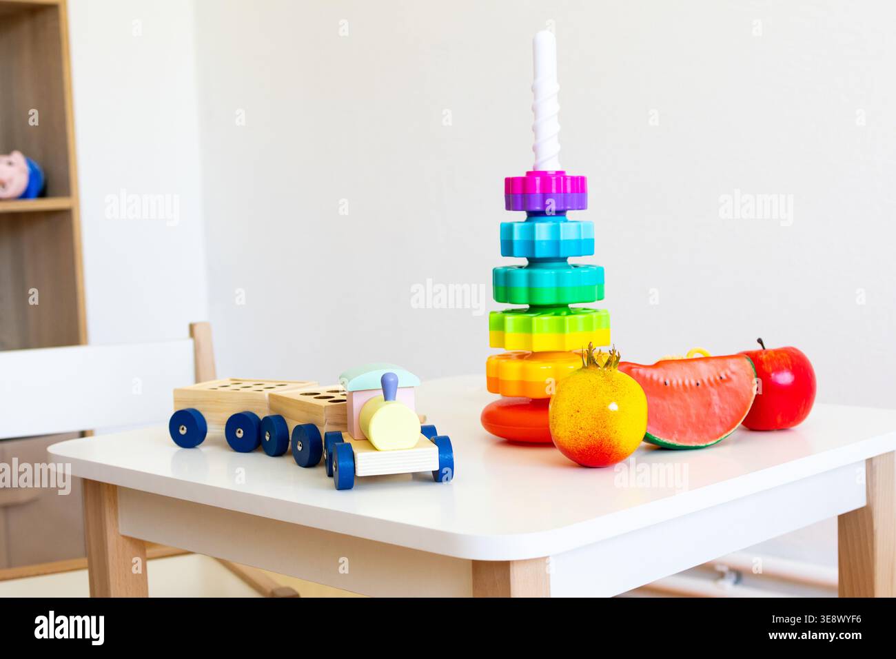 La torre dell'arcobaleno si erge accanto a un treno di legno e alla frutta giocattolo su un tavolo ordinato che offre oggetti colorati per contare la pratica del colore e fantasiosa Foto Stock