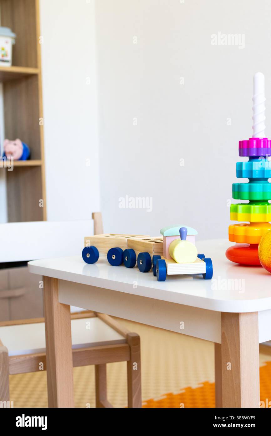 Un treno di legno pastello con due vagoni si trova vicino a un'alta torre arcobaleno su un tavolo per bambini, creando un angolo invitante per il gioco libero e presto Foto Stock