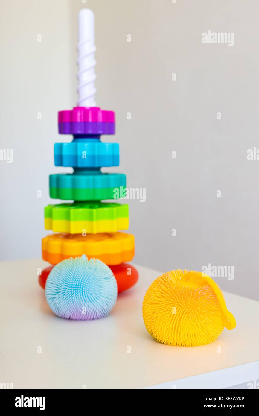 La torre Rainbow si erge su un tavolo con due morbide palline sensoriali che invitano i bambini a esplorare le texture, i colori e le sfide da impilare Foto Stock