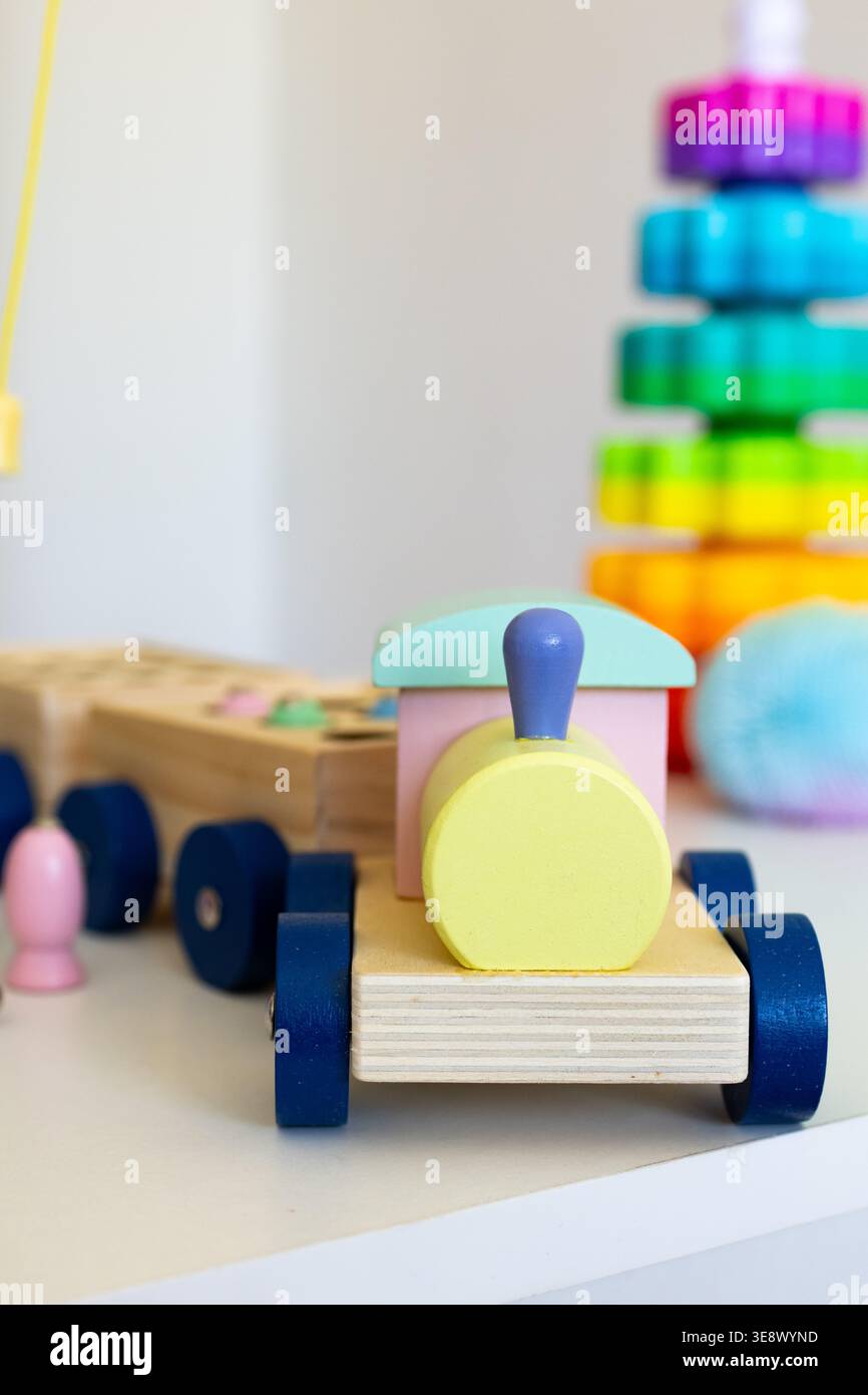 Vista ravvicinata di un motore in legno pastello con ruote blu su una scrivania per bambini che mostra la consistenza del legno naturale e colori amichevoli che incoraggiano i viaggi creativi Foto Stock