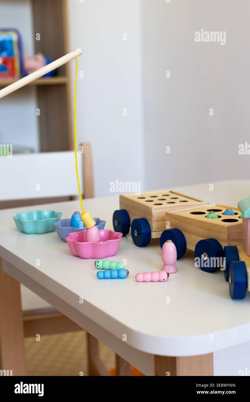Gioco di pesca magnetica in legno su un tavolo per bambini in una luminosa sala giochi con tazze pastello minuscoli pezzi di vermi e una tira lungo il carrello. Un allegro Montessori Foto Stock