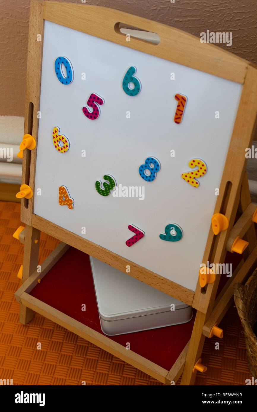 Un piccolo cavalletto in legno contiene una lavagna bianca con magneti colorati in un intimo angolo dell'aula. Un semplice gioco matematico incoraggia il conteggio dei riconoscimenti Foto Stock
