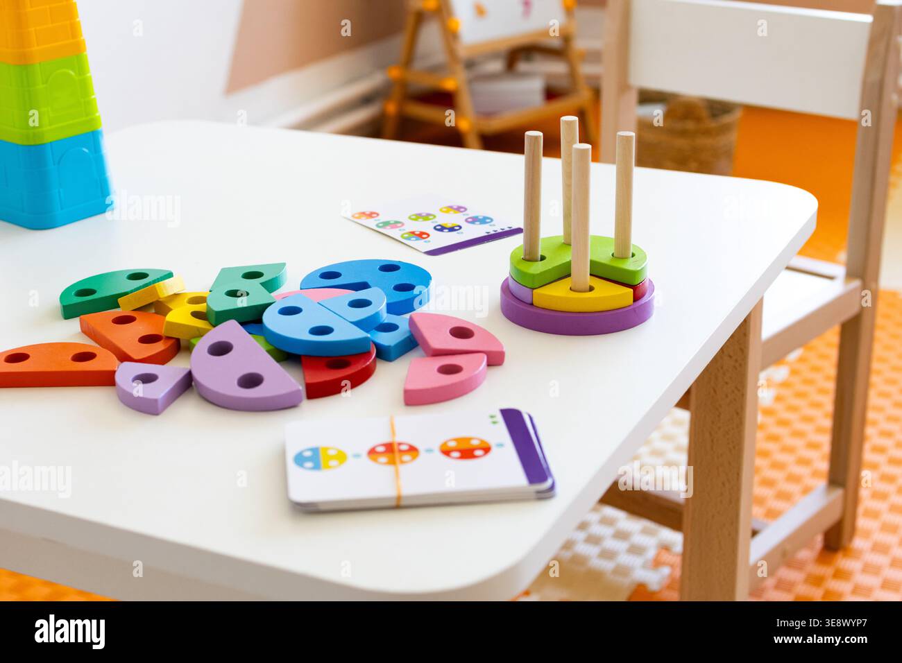 Un tavolo bianco regge una colorata smistatrice in legno con pioli e carte con motivi in una soleggiata aula. La riproduzione aperta supporta l'ordinamento dei colori corrispondenti Foto Stock