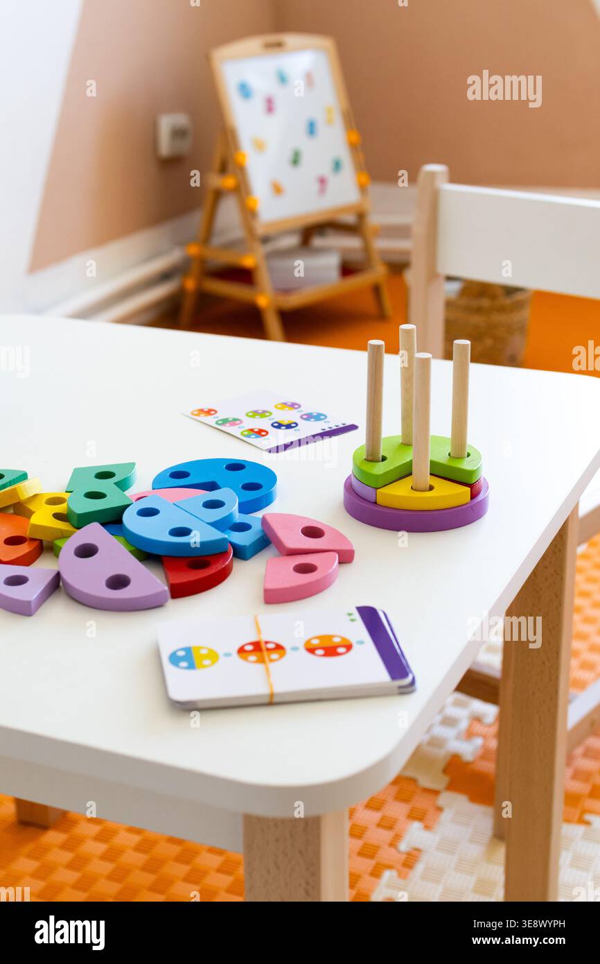 Pezzi colorati e una pedana si trovano su un tavolo pulito con una sedia per bambini, mentre un cavalletto si illumina delicatamente sullo sfondo. Un'installazione gioiosa Foto Stock
