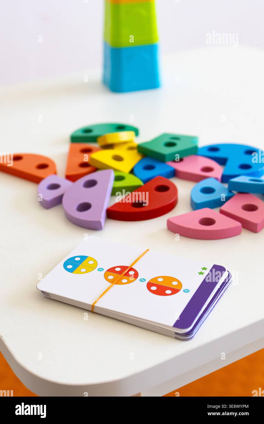 Le carte per le istruzioni e i pezzi di legno luminosi poggiano su un tavolo pulito invitando i bambini a costruire dei motivi sulla vicina pedana. Una scena vibrante Foto Stock